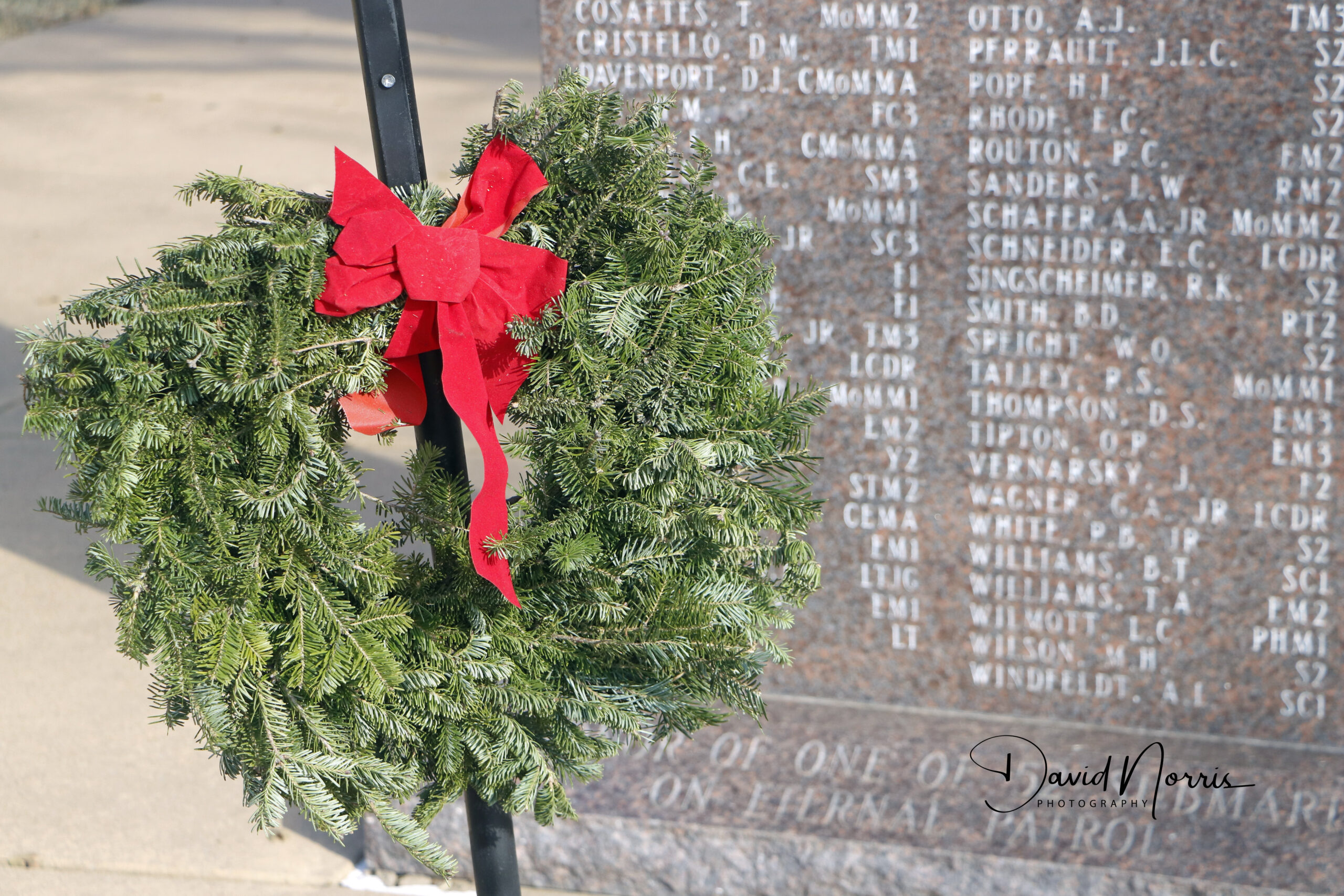 Wreath with red bow near engraved memorial.